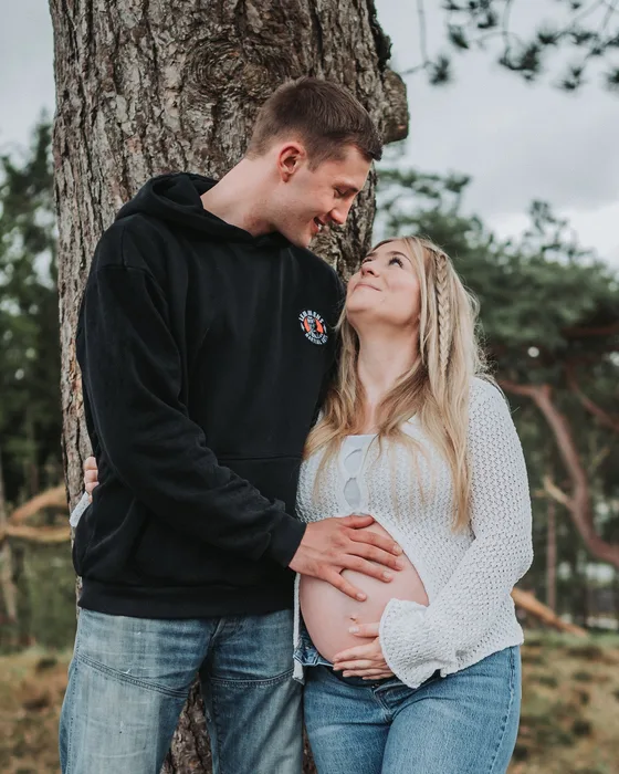 Werdende Eltern an einem Baum, er hält ihren Babybauch, bei einem Babybauchshooting in Dithmarschen