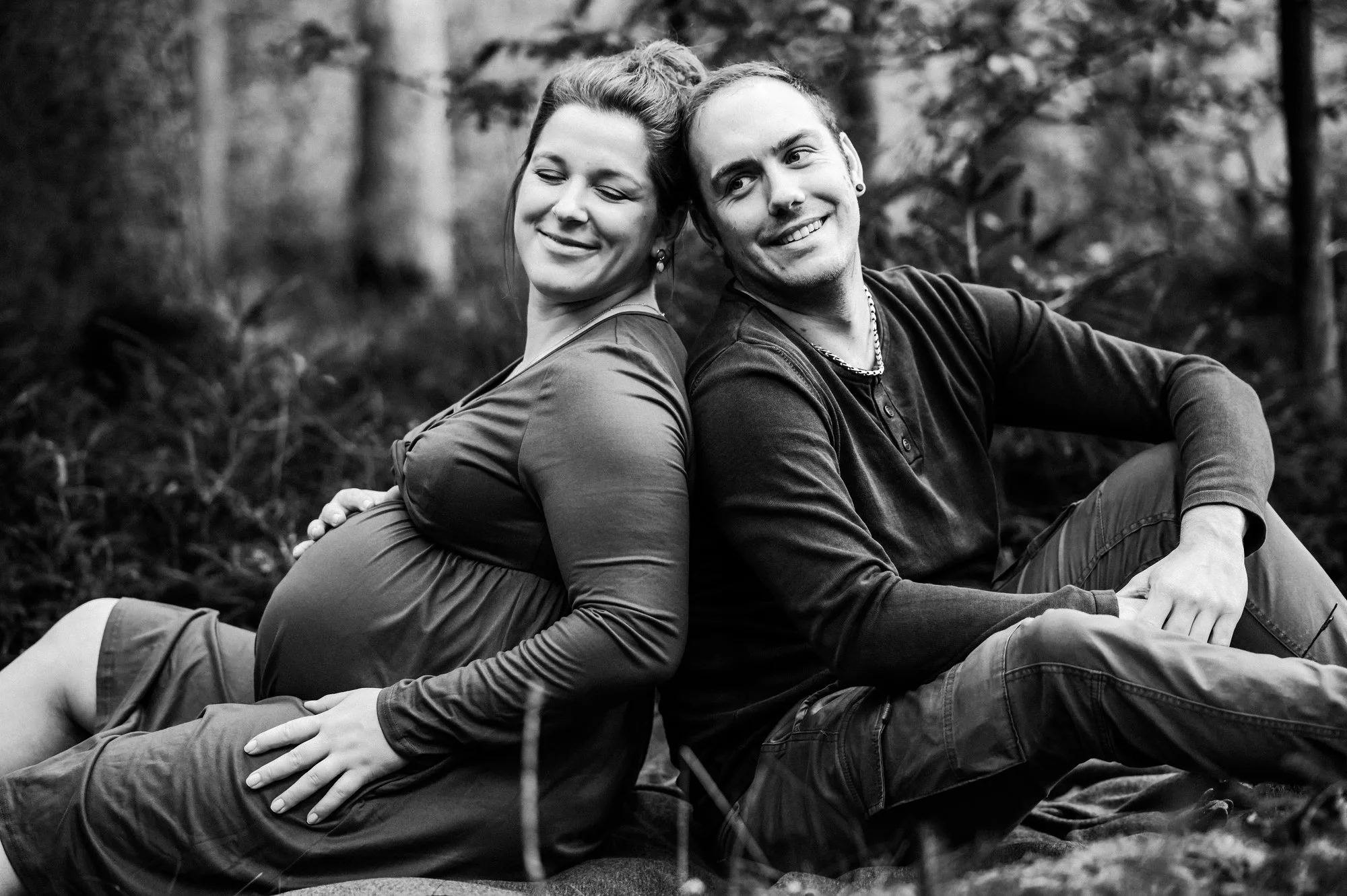 Werdende Eltern Rücken an Rücken, Schwarzweißfoto bei einem Babybauchshooting