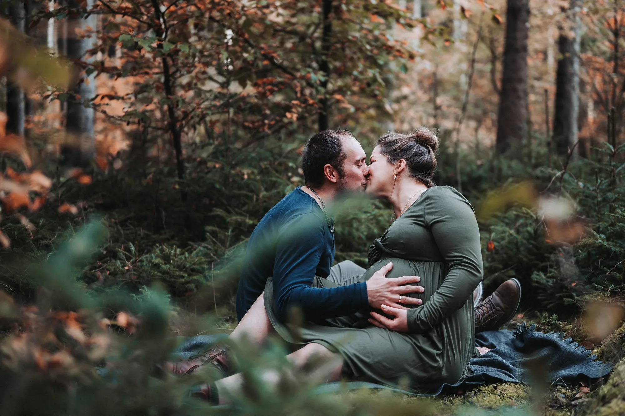 Werdende Eltern küssen sich im herbstlichen Wald bei einem Babybauchshooting